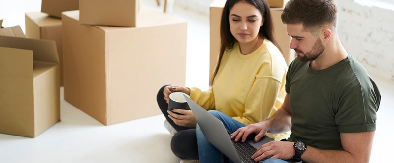 a couple is sitting on the floor and searching for something on a laptop