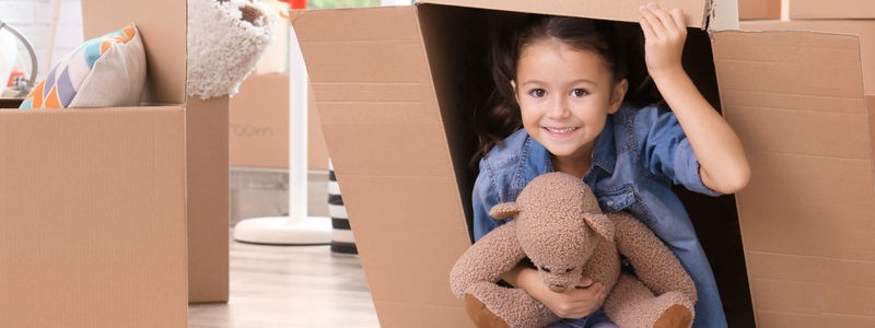 young kid with her teddybear under a cardboard box