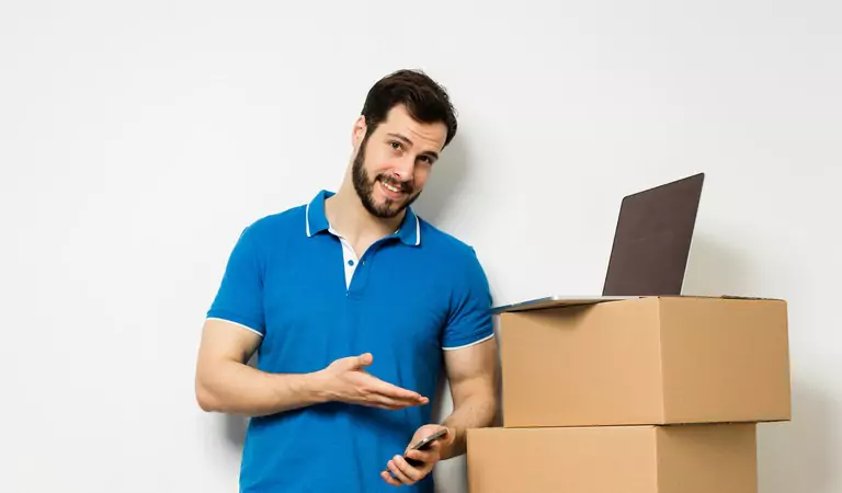 young man standing with a couple of cardboard boxes, laptop and a phone