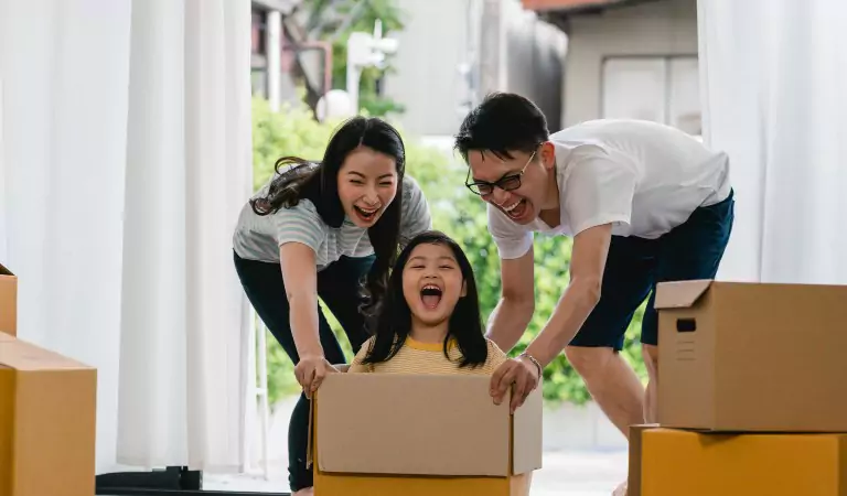 young kid sitting in a cardboard box and parents pushing it from the back