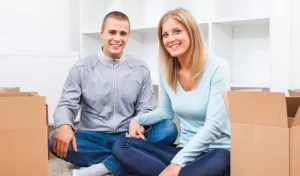 couple sitting inside of a house with some cardboard boxes