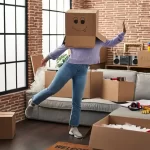 Woman in t-shirt and blue jeans covered her face with a moving box.