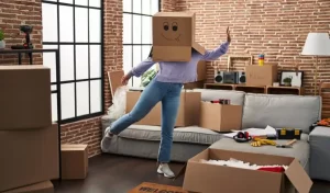 Woman in t-shirt and blue jeans covered her face with a moving box.