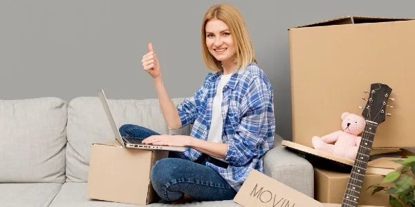 Woman in check shirt sitting on sofa with her laptop showing her thumps up.