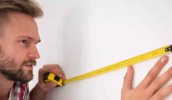 young man with an inchtape measuring a wall
